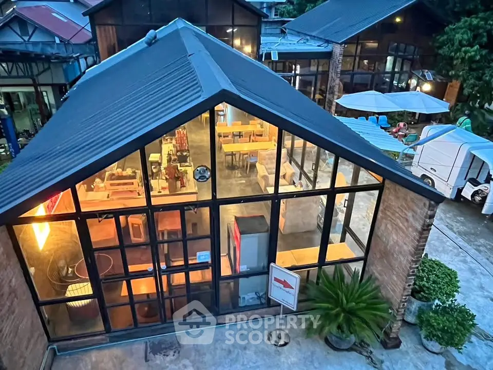 Modern industrial-style building with large glass windows and outdoor seating area.
