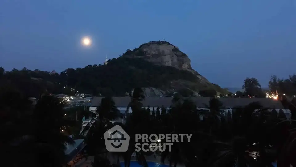 Scenic evening view of a hill with moonlight, surrounded by lush greenery and distant ocean.