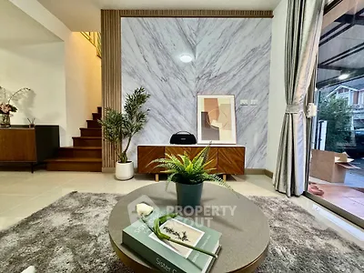 Stylish living room with modern decor, featuring a cozy rug, elegant furniture, and a view of the staircase.