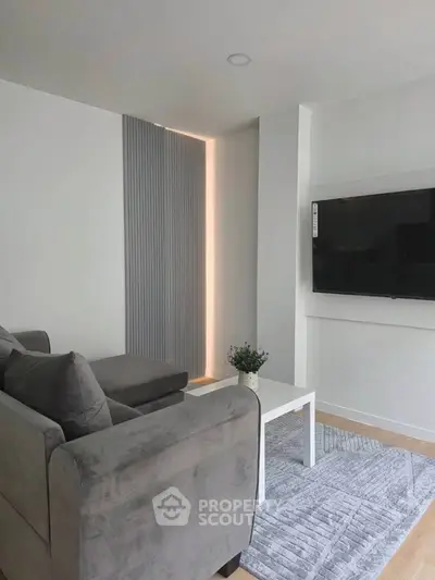 Modern living room with sleek gray sofa, wall-mounted TV, and stylish decor in a contemporary apartment.
