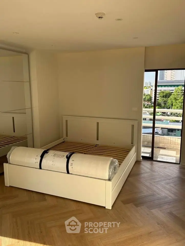 Spacious bedroom with large window and wooden flooring in modern apartment