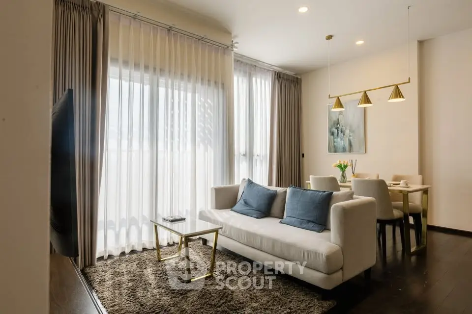 Elegant living room with modern decor and dining area, featuring large windows and stylish lighting.