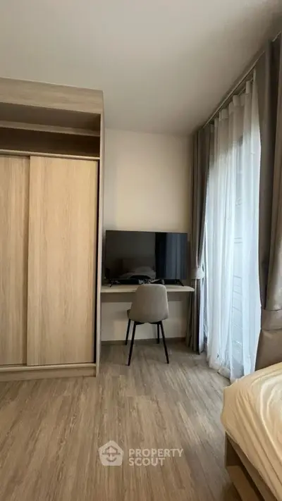 Modern bedroom with TV and wardrobe, featuring sleek wooden flooring and natural light.