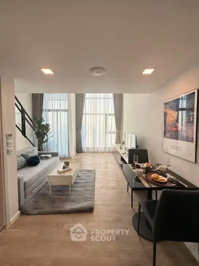 Modern living room with stylish decor and dining area, featuring large windows and natural light.