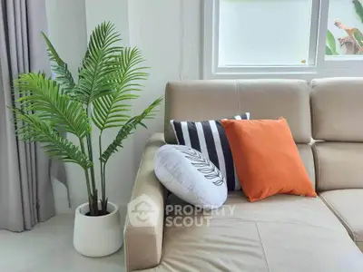 Modern living room with stylish sofa and decorative cushions, featuring a lush indoor plant by the window.