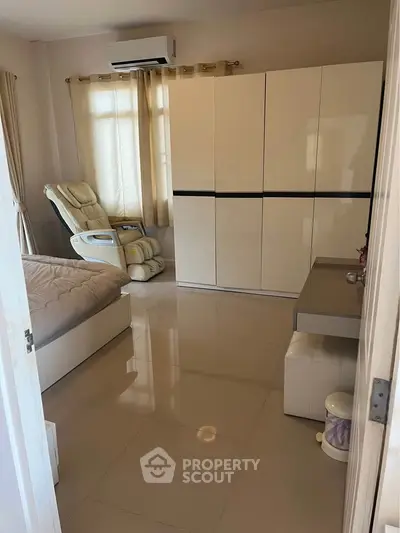 Spacious bedroom with modern furniture and air conditioning, featuring a sleek wardrobe and comfortable seating.