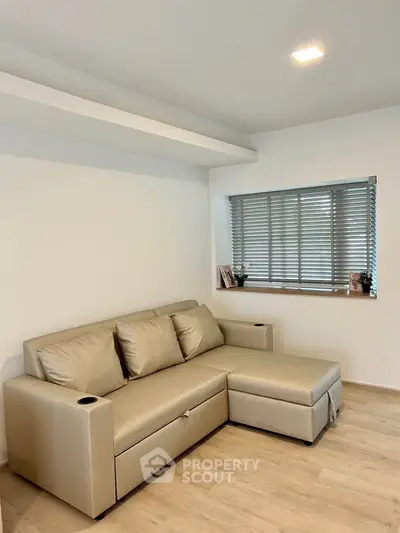 Modern living room with beige sectional sofa and large window with blinds.