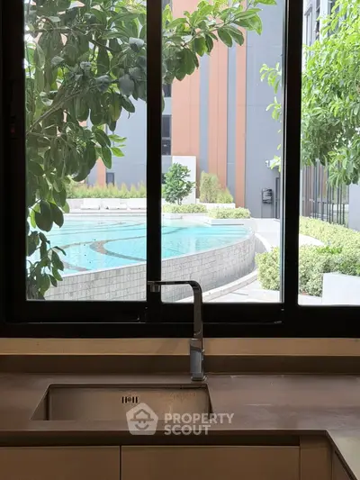 Modern kitchen with sleek sink overlooking serene pool and lush greenery through large window.