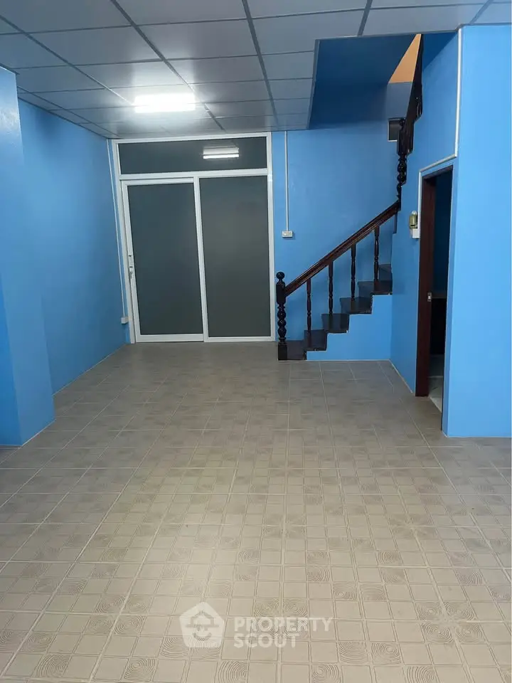Spacious blue-walled interior with staircase and tiled flooring, ideal for versatile living space.