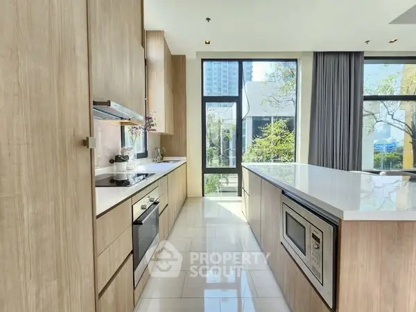 Modern kitchen with sleek wooden cabinets and large windows offering natural light.