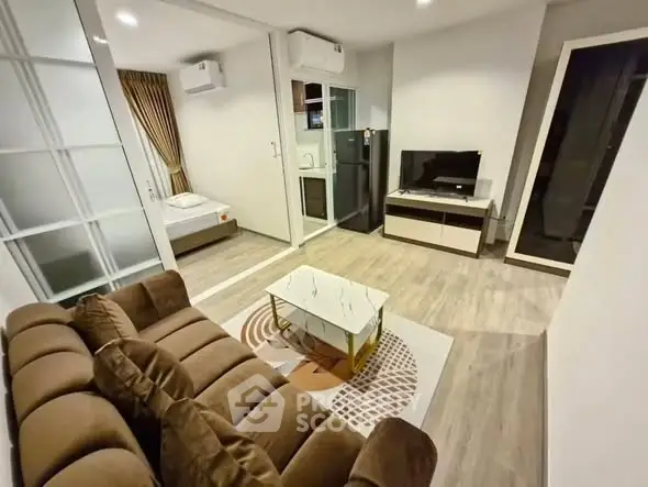 Modern living room with cozy sofa, TV, and open view to bedroom and kitchen.