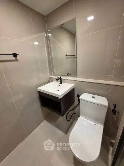 Modern bathroom with sleek fixtures and neutral tiles, featuring a wall-mounted sink and toilet.