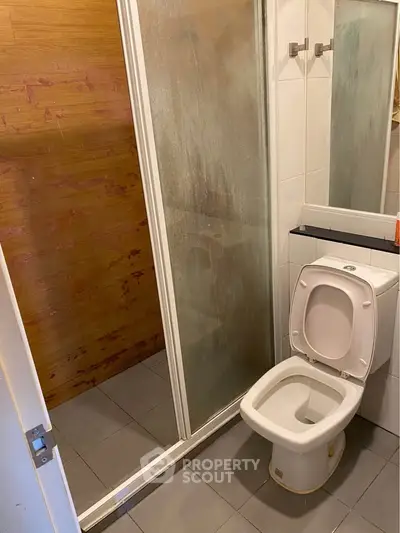 Compact bathroom with shower and toilet, featuring a modern design and tiled flooring.
