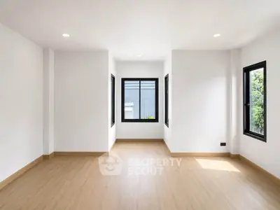 Spacious and bright empty room with large windows and wooden flooring, perfect for customization.