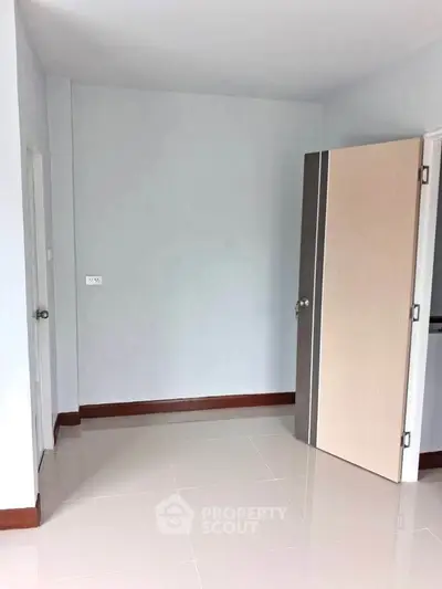 Spacious empty room with glossy tiled floor and open door, ready for customization.