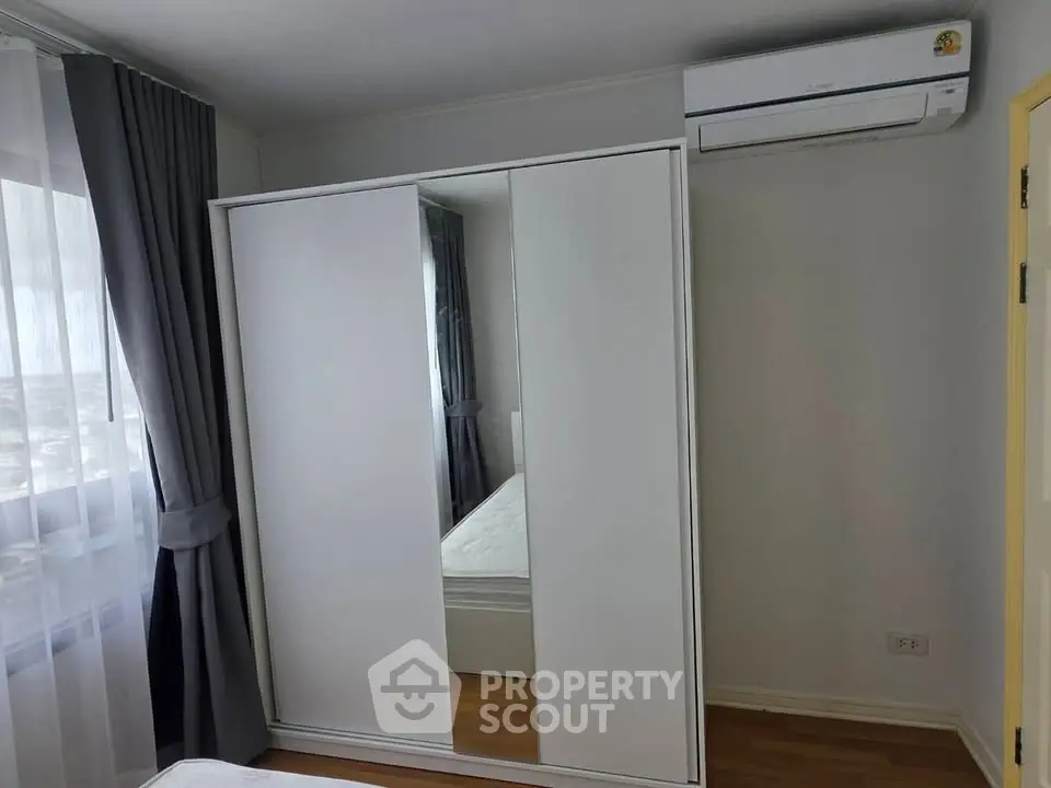 Modern bedroom with sleek wardrobe and air conditioning, featuring large window with city view.