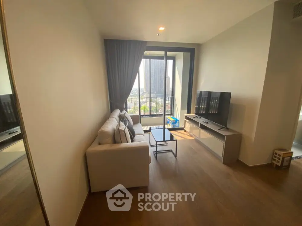 Modern living room with large window and city view, featuring cozy sofa and flat-screen TV.