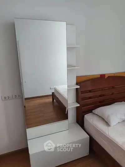Modern bedroom with sleek wooden flooring and stylish bed frame, featuring a large mirror and storage shelves.