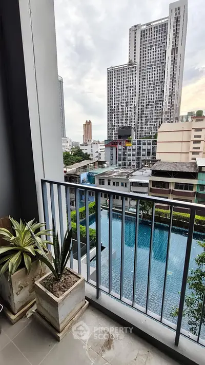 Modern balcony with city view overlooking a pool, featuring potted plants and sleek railing.