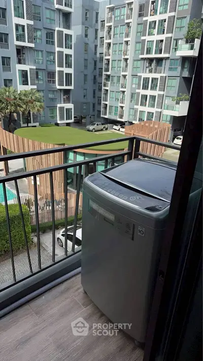 Modern apartment balcony with washing machine overlooking pool and garden view.