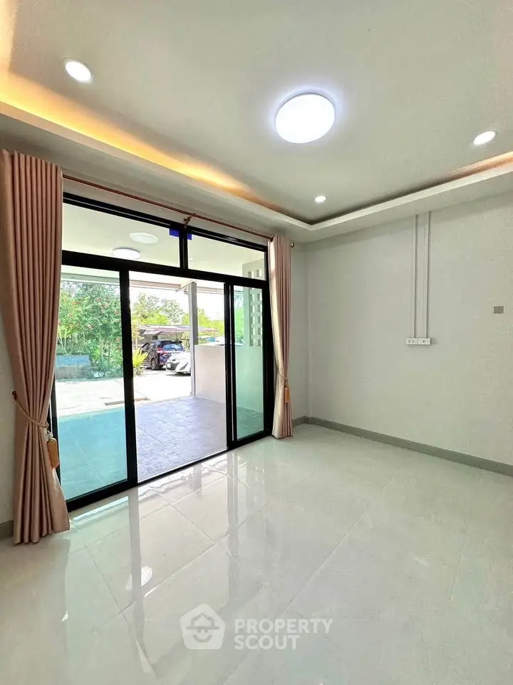 Spacious living room with sliding glass doors leading to a balcony, featuring modern lighting and elegant curtains.