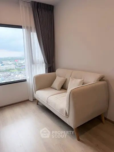 Cozy living room with a beige sofa and city view from large window.
