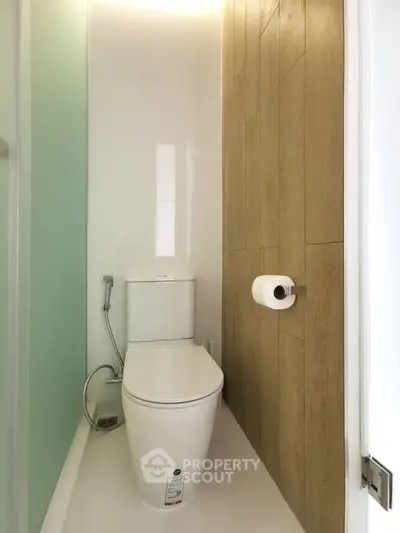 Modern minimalist bathroom with sleek toilet and wood panel accent wall.