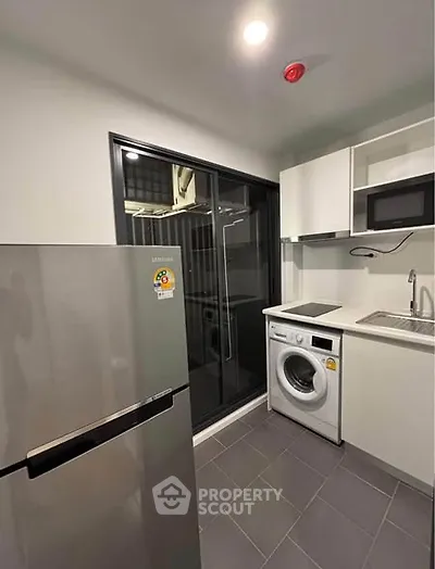 Modern kitchen with sleek appliances including fridge, washing machine, and microwave in compact layout.
