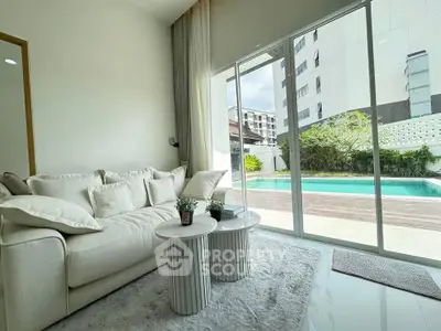 Luxurious living room with pool view, featuring elegant white sofa and modern decor, perfect for relaxation.