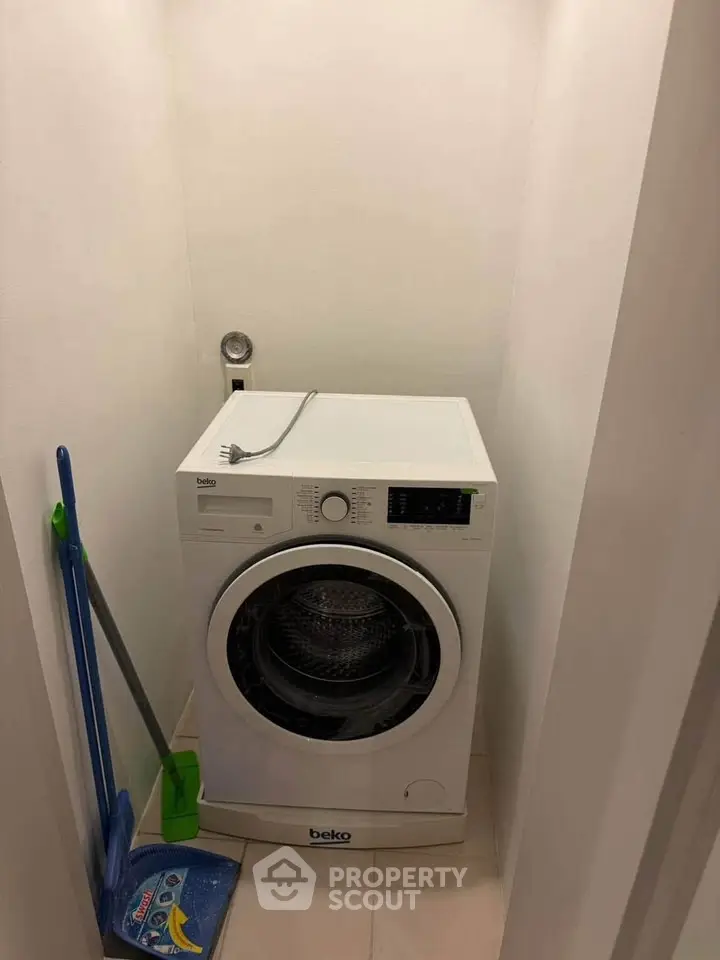 Compact laundry nook with washing machine and cleaning tools in modern apartment.