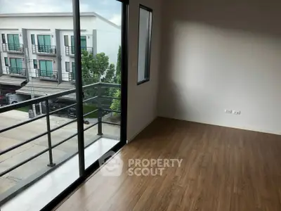 Spacious empty room with wooden flooring and large windows overlooking modern townhouses.