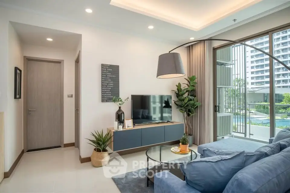 Modern living room with stylish decor and large windows overlooking a pool view, featuring a cozy blue sofa and sleek TV unit.