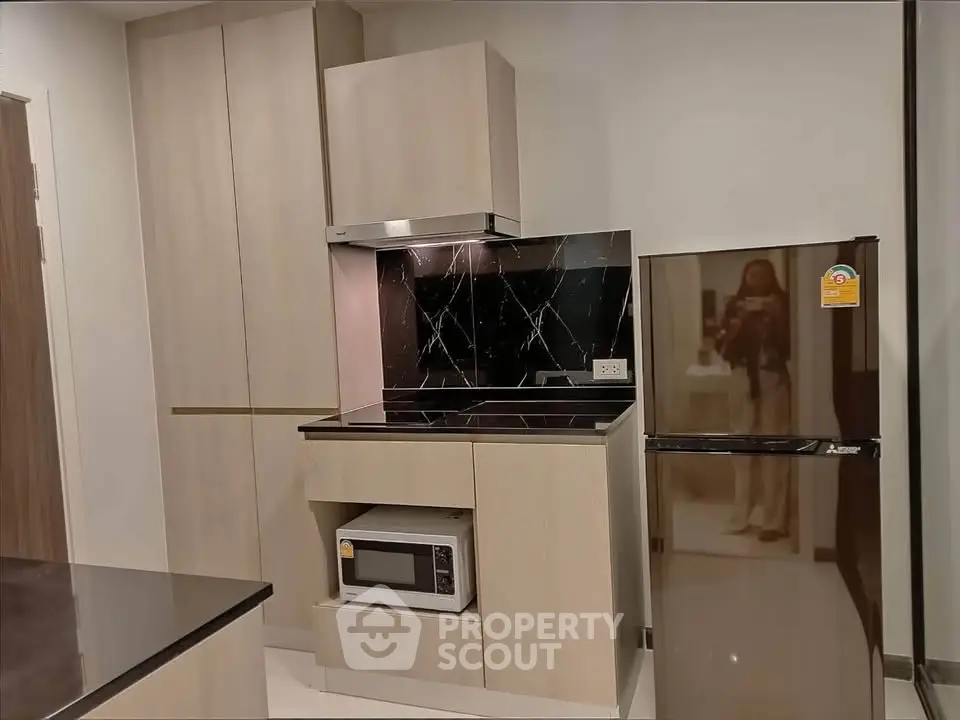 Modern kitchen with sleek cabinetry, microwave, and fridge in stylish apartment.