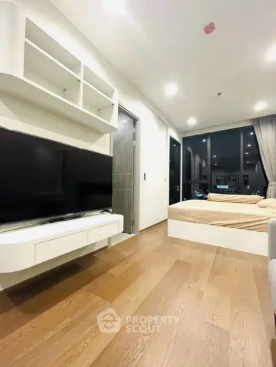 Modern living room with large TV and cozy bed, featuring sleek wooden flooring and ambient lighting.