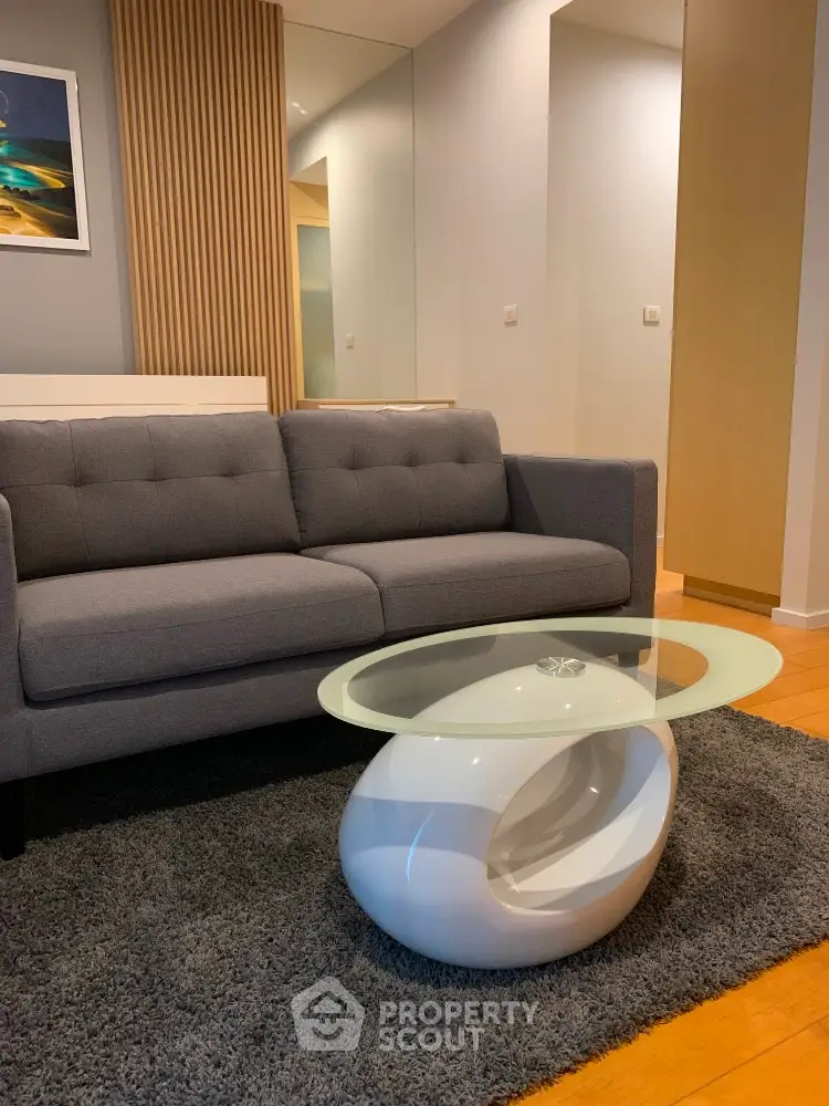 Modern living room with stylish gray sofa and unique glass coffee table on plush rug.