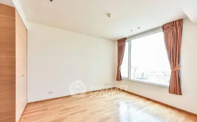 Spacious empty bedroom with large window and wooden flooring