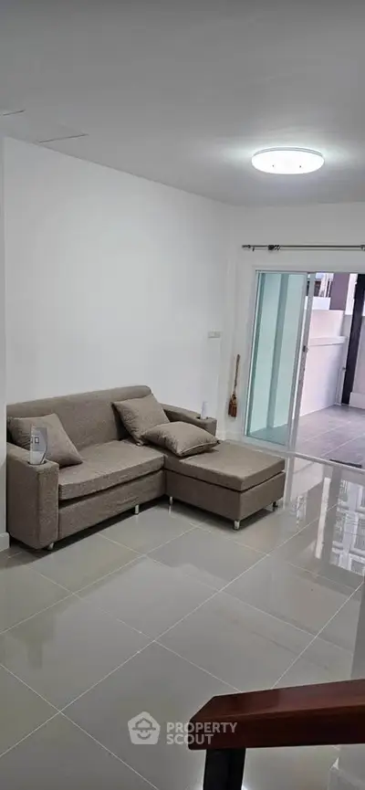 Modern living room with sleek sofa and glossy tiled floor, leading to a bright balcony area.