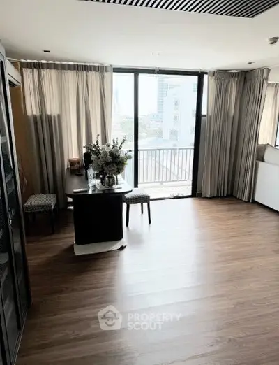 Spacious living room with large windows and balcony access, featuring elegant decor and wooden flooring.