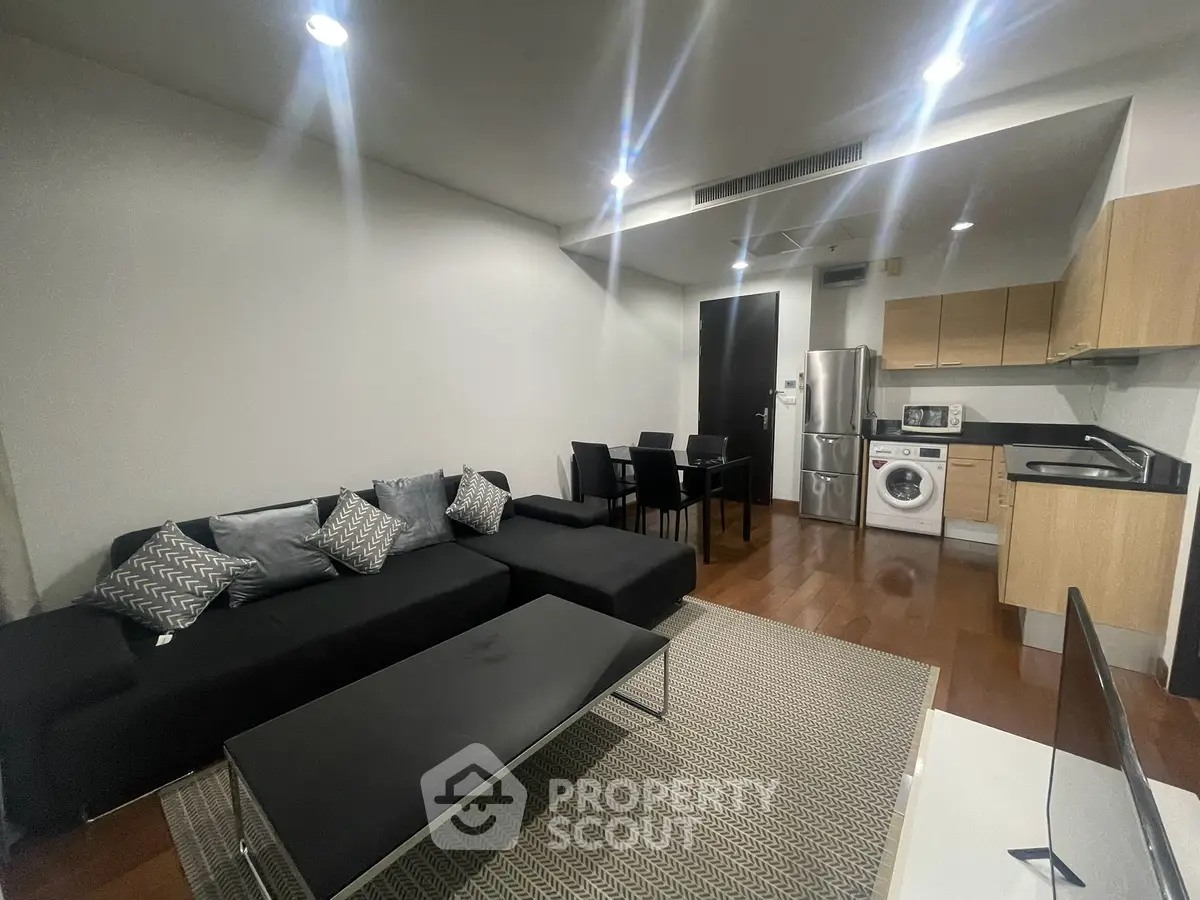 Modern living room with sleek kitchen and dining area, featuring a washing machine and stylish furniture.