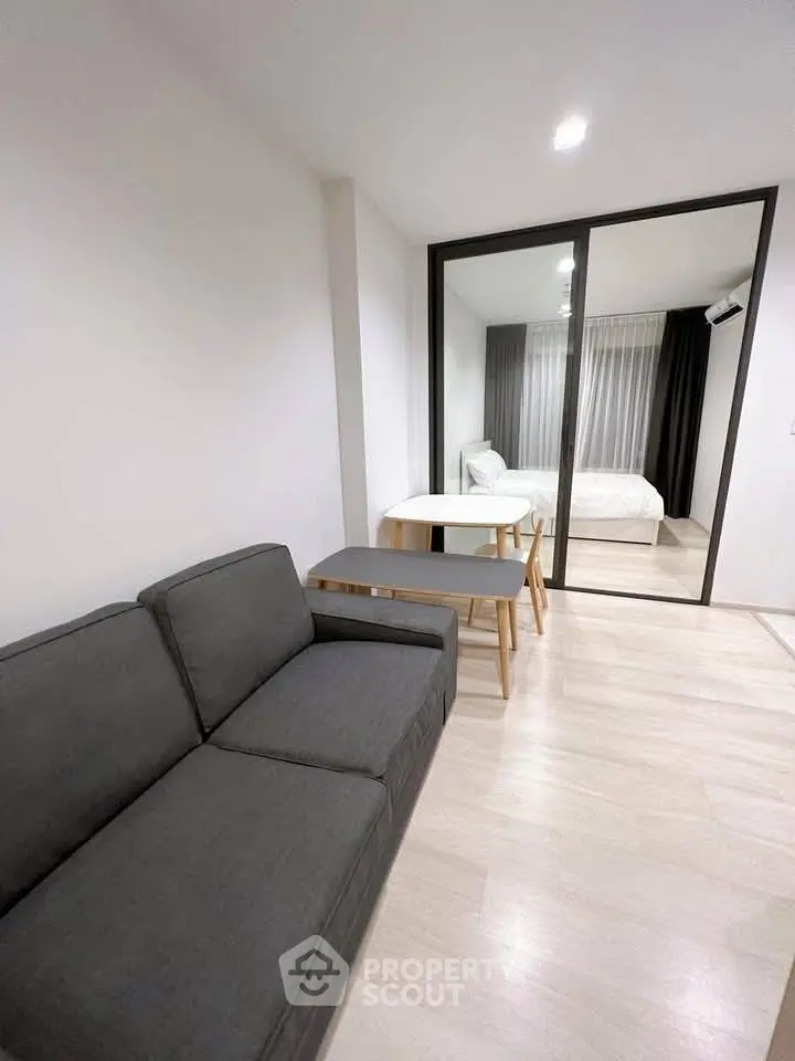 Modern apartment with sleek living room and cozy bedroom separated by glass partition.