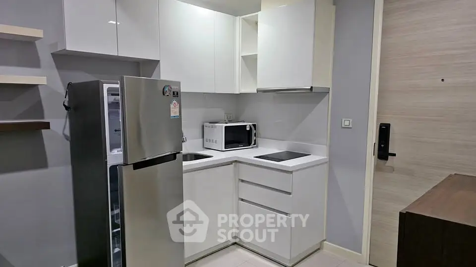 Modern compact kitchen with sleek white cabinets and stainless steel appliances in a stylish apartment.