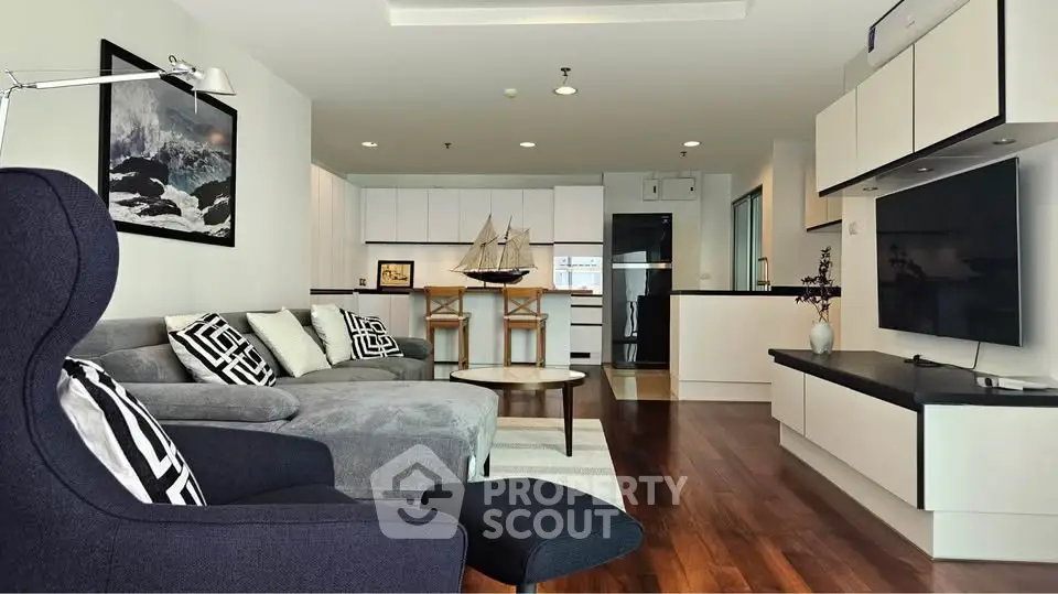 Modern living room with stylish decor and open kitchen layout, featuring sleek furniture and hardwood floors.