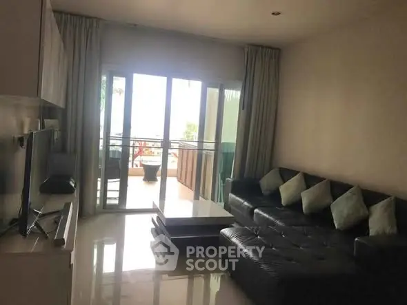 Spacious living room with modern black leather sofa and large glass doors leading to balcony.