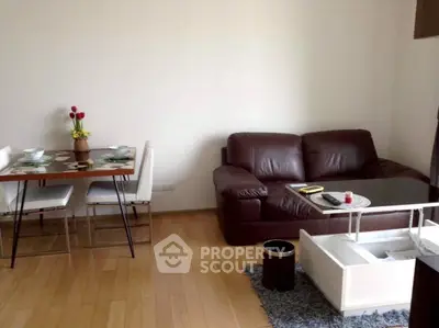 Cozy living room with leather sofa and dining area on wooden flooring.