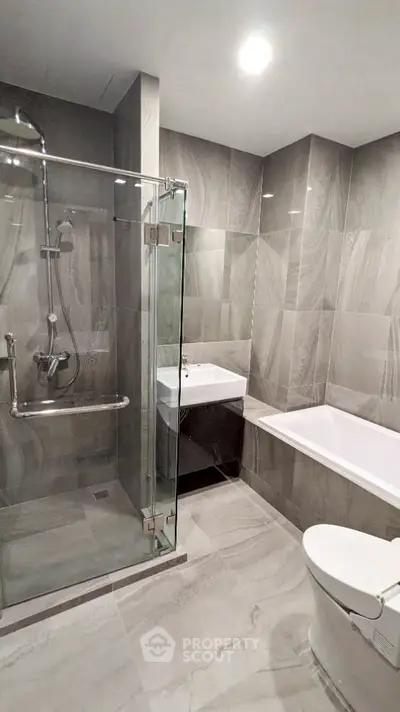 Luxurious modern bathroom with glass shower and bathtub in elegant gray tiles.