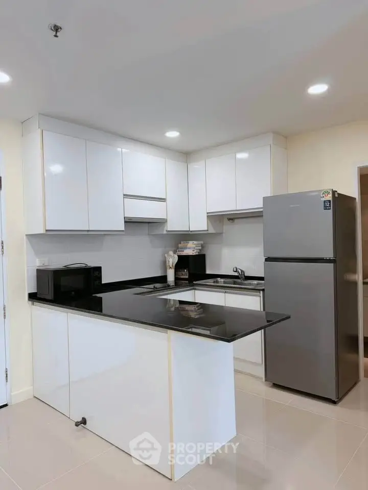 Modern kitchen with sleek white cabinets and black countertops, featuring a stainless steel fridge and microwave.