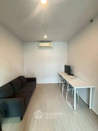 Modern living room with sleek sofa and workspace, featuring air conditioning and minimalist design.