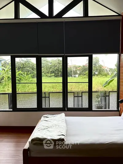 Spacious bedroom with large windows offering serene water and garden views.
