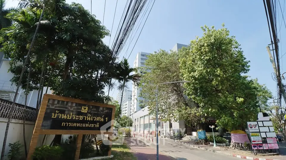 Charming residential building entrance with lush greenery and clear blue sky.