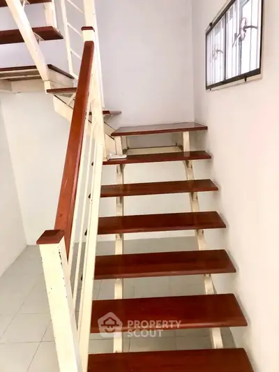Modern wooden staircase with sleek design and white railing in a bright interior space.